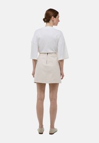 T-shirt blanc surdimensionné à manches courtes associé à une jupe A en beige avec une fente arrière et un détail de fermeture éclair visible.