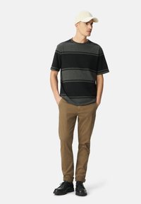 Zwart en grijs gestreepte short-sleeve shirt, beige pet, kaki broek en zwarte schoenen. Eenvoudig ontwerp met effen kleuren en subtiele horizontale patronen.