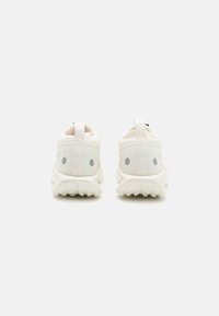 zapatillas ligeras de color crema con un acabado texturizado, patrones sutiles en la parte trasera y una suela de goma blanca con diseño.