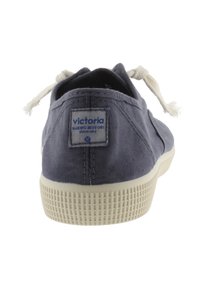 Zapatillas de lona navy con suela de goma blanca, con un parche de logo en el talón y cordones color crema. Tejido texturizado con detalles de costura.