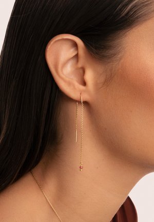 Boucles d'oreilles en chaîne dorée avec un design en barre élancée et un petit accent en perle colorée, suspendues gracieusement au lobe de l'oreille.