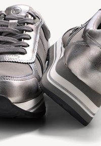 Baskets gris métallisé avec une tige en cuir à la texture lisse, un bout arrondi et une semelle extérieure rayée en noir et blanc contrastant.