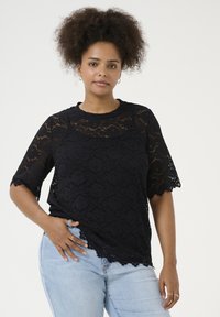 Black lace top with short, scalloped sleeves, featuring floral patterns and a round neckline. Paired with light blue jeans.