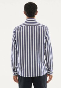 Camicia a maniche lunghe con strisce verticali blu e bianche, polsini con bottoni, colletto classico e orlo posteriore dritto. Realizzata in tessuto intrecciato.