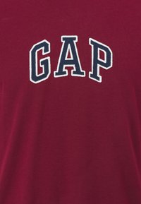 T-shirt bordeaux avec logo "GAP" brodé en blanc et bleu marine. Tissu doux, manches courtes, encolure ronde et coupe décontractée.