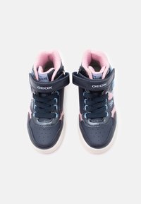 Jūras zila un rozā augstās tenisa kurpes ar velcro siksniņu, teksturētu ādu, perforētu purngalu un ziliem šņorēm, kas radītas ērtībai un gaisa caurlaidībai.