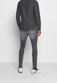 Gray textured shirt with a curved hem, paired with slim-fit gray jeans. Footwear features a mix of black, white, and turquoise accents.