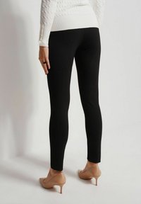 Czarne legginsy wykonane z elastycznego materiału, o dopasowanym kroju. Połączone z białym swetrem o fakturze i beżowymi szpilkami.