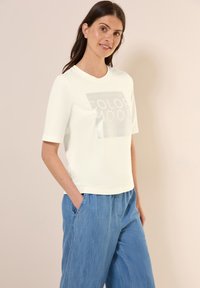 T-shirt clair à manches courtes avec un graphique brillant "COLOR MOOD" sur le devant. Assorti avec un pantalon en denim bleu ample.