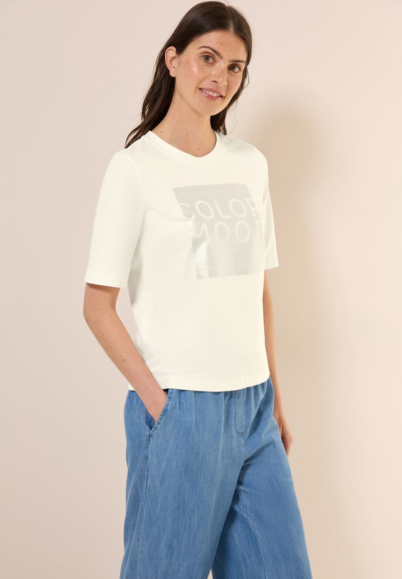 T-shirt clair à manches courtes avec un graphique brillant "COLOR MOOD" sur le devant. Assorti avec un pantalon en denim bleu ample.