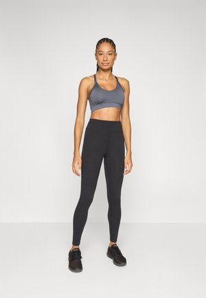 Športni modrček sive barve, kombiniran s črnimi legicami z visokim pasom. Obe sta narejeni iz raztegljivega materiala. Obutev so črni športni copati.