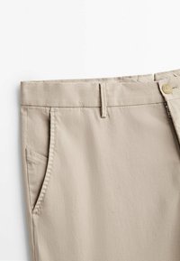 Beige katoenen broek met een vlak voorkant, ritssluiting, twee zijzakken en een subtiele textuur in de stof. Heeft een klassieke tailleband met een knoop.