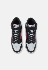 Korkeat Nike-tennarit, joissa on musta nahka, valkoinen kärki, vaaleanpunaiset sivuakkentit ja harmaat nauhat, joissa on rei'itettyä yksityiskohtaa yläosassa.