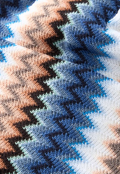 Gros plan d’un tissu tricoté avec un motif en zigzag dans des nuances de bleu, marron, noir, blanc et vert clair.