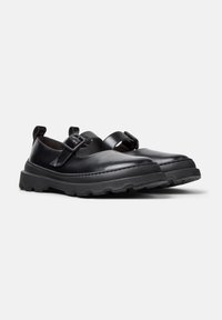 Zwarte leren Mary Jane schoenen met gespbanden, stevige rubberen zolen en treklussen, gepresenteerd op een witte achtergrond.