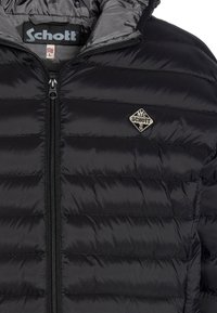 Doudoune noire à motifs matelassés, avec une fermeture éclair sur toute la longueur et un petit logo brodé sur le côté gauche de la poitrine.