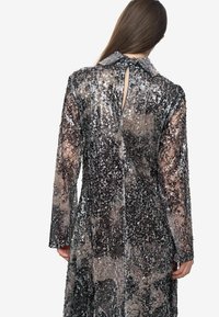 Abito lungo con paillettes dal finish lucido, caratterizzato da un design con colletto, maniche lunghe e un dettaglio a chiave sul retro, in toni di argento e nero.