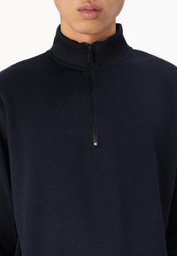 Pullover navy a mezza zip realizzato in materiale morbido, con colletto alto e zip texturizzata. Design semplice e minimalista senza motivi.