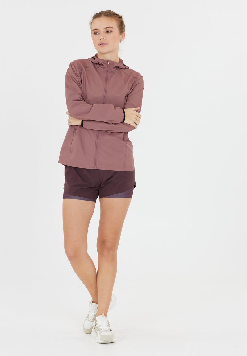 Lichtgewicht mauve jack met een capuchon en een rits aan de voorkant; gevormd ontwerp. Gepaard met donkerpaarse shorts en witte sneakers.