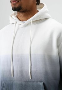 Wit naar grijs verloop hoodie met een voorzak. Voorzien van trekkoorden en een zachte, gestructureerde stof. Eenvoudig ontwerp met een comfortabele pasvorm.