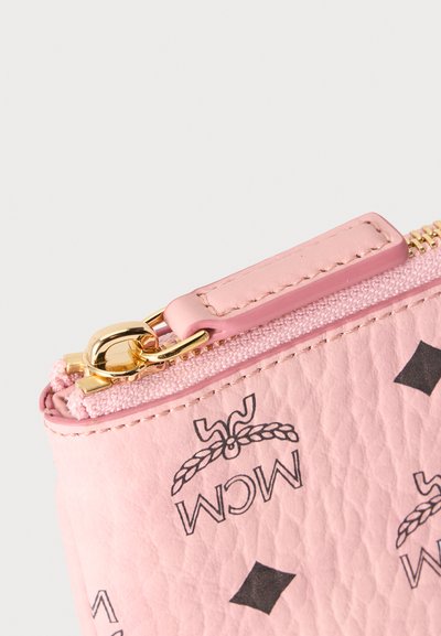 Gros plan d'une pochette en cuir texturé rose avec logos MCM noirs, fermeture éclair dorée et tirette de fermeture assortie rose.