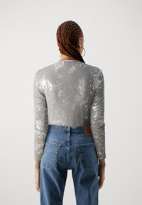Long-sleeve top in light gray with a shiny, textured pattern; paired with high-waisted blue jeans featuring stitched back pockets.