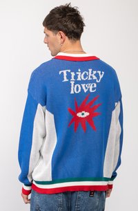 Pulover din tricot cu bază albastră, accente roșii și mâneci albe. Text grafic 'Tricky love' cu un design ascuțit roșu pe spate.