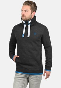 Sweatshirt en polaire gris foncé avec un col haut, des cordons blonds blancs et bleus, et des accents bleus aux poignets et à l'ourlet. Comprend des poches avant.