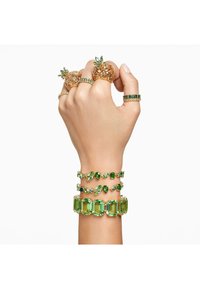 Gold and green gemstone jewelry: three stacked bracelets with green stones, and multiple rings, including pineapple-shaped designs.