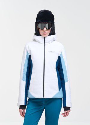 Personne portant une veste de ski blanche et bleue, un pantalon turquoise, de grandes lunettes de ski noires et un bonnet d'hiver noir doublé de fourrure sur un fond uni.