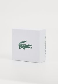 Boîte blanche avec une surface texturée, arborant un logo de crocodile vert sur le devant et un autre marquage sur le côté.