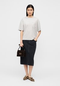 Γκρι κοντομάνικη μπλούζα με τσέπη στο στήθος, μαύρη φούστα από τζιν και παπούτσια τύπου slip-on με λεοπάρ σχέδιο. Κρατά μια μικρή καφέ σκούρα τσάντα χειρός.