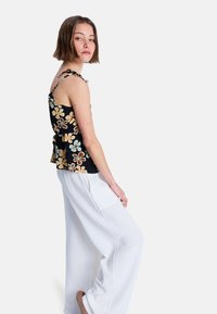Czarny top na ramiączkach w kwiaty w jasnoniebieskim i kremowym kolorze, zestawiony z luźnymi białymi spodniami i okrągłym dekoltem. Materiał o strukturze i regulowane ramiączka.