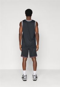 Top atlético preto com bainha branca, combinado com calções pretos com uma bainha de padrão multicolorido, acompanhado de ténis brancos e pretos.