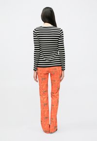 Čierno-biele pruhované tričko s dlhým rukávom skombinované s oranžovými rozšírenými nohavicami s kvetinovým vzorom a jemnými sivými akcentmi, zobrazené zozadu.