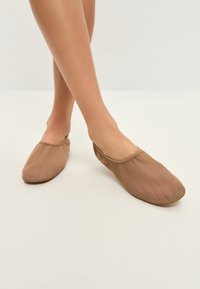Zapatillas ligeras y de poner en color beige, fabricadas en material de malla con punta redondeada. Textura suave, diseño flexible y detalles de costura minimalista.