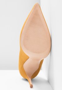 Chaussure à talon aigu en suede jaune avec un bout pointu, un talon stiletto mince et une semelle en caoutchouc texturé. Design minimaliste avec une finition lisse.