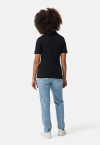 Svart kortärmad tät t-shirt och ljusblå jeans, med avslappnad passform och uppvikta fållar, i kombination med vita sneakers.