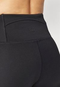 Des leggings noirs taille haute en matière extensible qui présentent des coutures plates et un logo sur la taille, soulignant une silhouette lisse.
