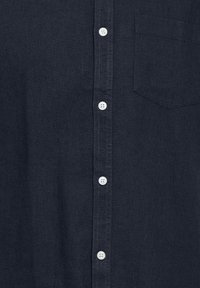 Camisa abotonada de color azul oscuro hecha de un tejido texturizado con un pequeño bolsillo en el pecho. Presenta botones blancos y un diseño de cuello clásico.