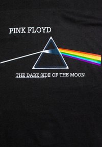 Černé tričko s grafickým motivem hranolu, ze kterého vychází duhový paprsek. Text zní „PINK FLOYD“ a „THE DARK SIDE OF THE MOON“.