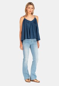 Granatowa bluzka bez rękawów z marszczonym wykończeniem i okrągłym dekoltem, połączona z jasnoniebieskimi dżinsami w kształcie dzwonów i brązowymi klapkami.