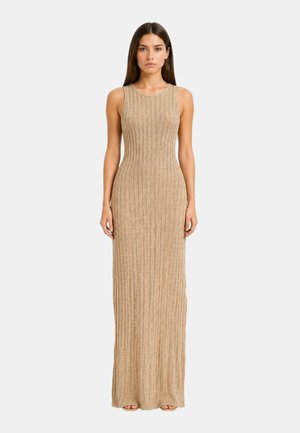 Donna in piedi di fronte indossa un vestito lavorato a maglia beige, senza maniche e lungo fino ai piedi, con motivo a coste.