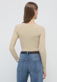 Beige geripptes Langarmoberteil mit taillierter Passform, kombiniert mit hochgeschnittenen blauen Jeans aus Denim, die einen schwarzen Ledergürtel und klassische Taschen besitzen.