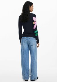 Long-sleeve navy top with large pink floral design on the left arm, paired with wide-leg light denim jeans featuring a faded finish.