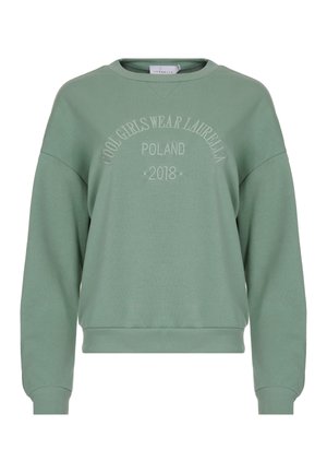 Zaļš džemperis ar noapaļotu kakla izgriezumu un ripinātām piedurknēm. Tam ir uzspiedis teksts: "FORŠĀS MEITENES VALKĀ LAURELLA POLAND 2018."