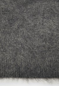 Primo piano di un tessuto fuzzy morbido, grigio scuro, con fibre visibili e una texture leggermente irregolare su uno sfondo bianco.