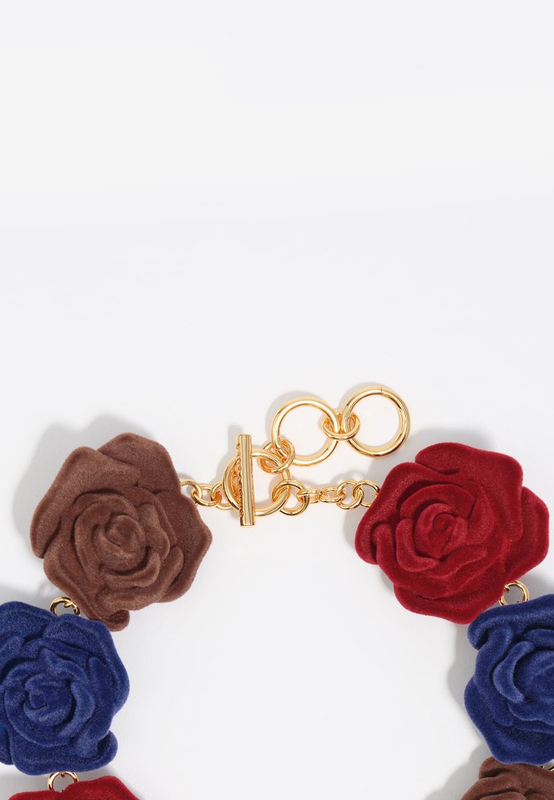 Collar floral colorido con pétalos en forma de rosa en materiales de terciopelo marrón, rojo y azul. Presenta herrajes en tono dorado y un cierre de palanca.