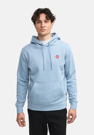 Hellblaue Kapuzenpullover aus weichem Stoff, mit einer Fronttasche und einem kleinen roten Logo auf der Brust. Pullover-Design.