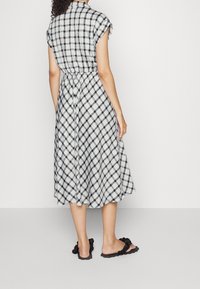 Černobíle kostkované šaty s páskem v pase, krátkými rukávy a délku po kolena, doplněné černými texturovanými nazouvacími sandály.